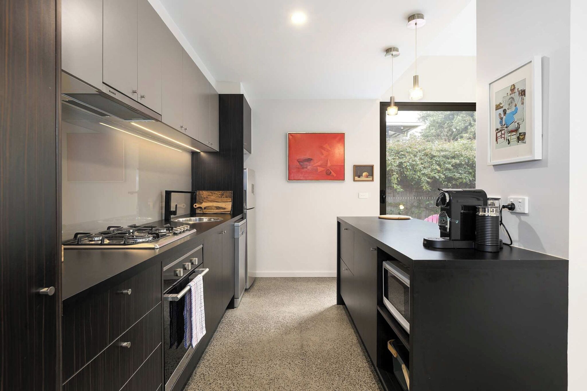 A modern kitchen with dark cabinetry, stainless steel appliances, and a coffee machine on the counter.