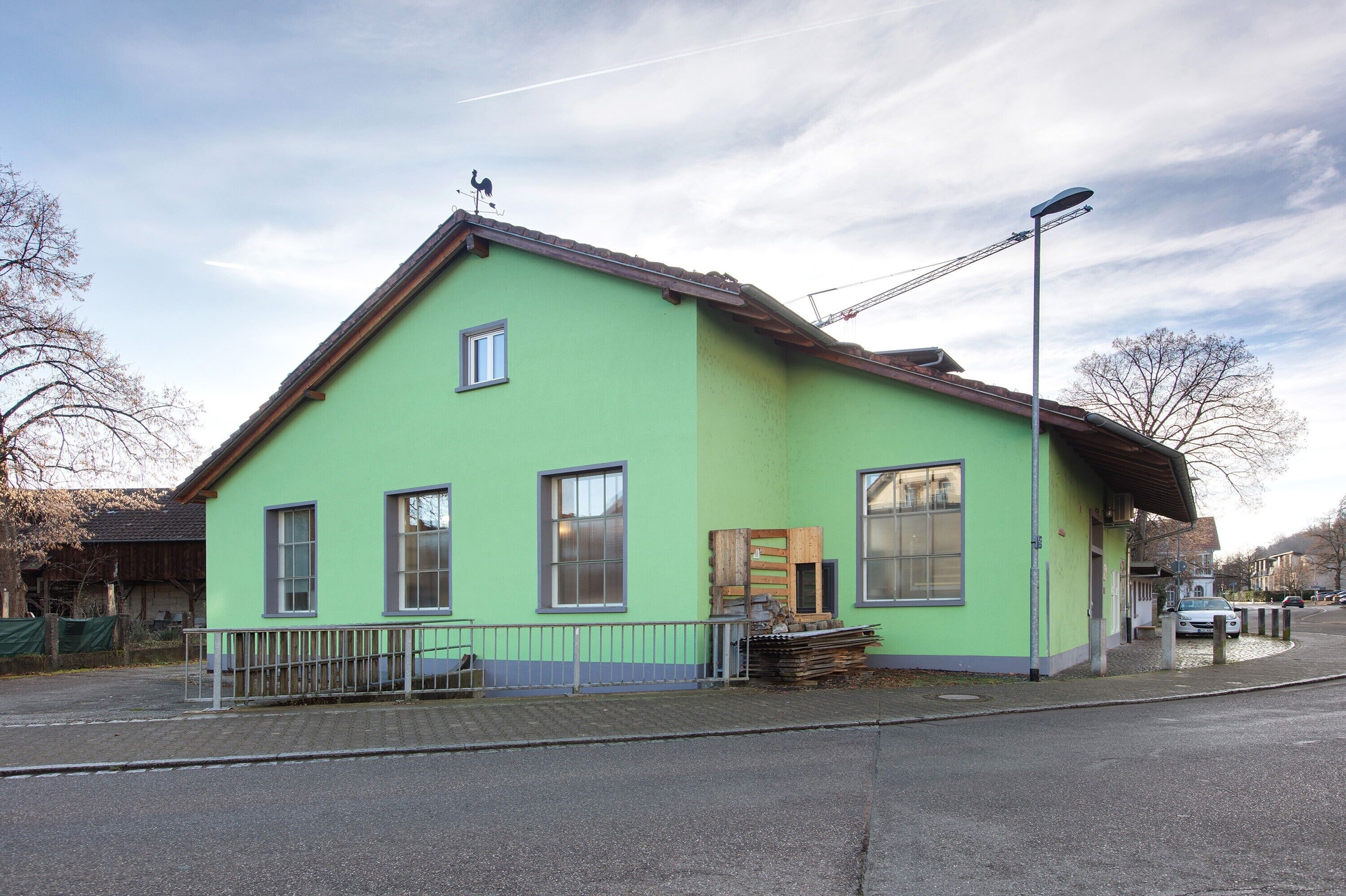 Un edificio verde con techo inclinado, una ventana pequeña y una farola.