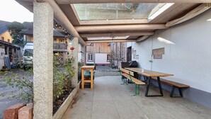 An outdoor patio with a wooden table and benches, a glass enclosure, and a view of the street. - Apartment "Atelier" with Private Terrace and Wi-Fi (Schopfheim)