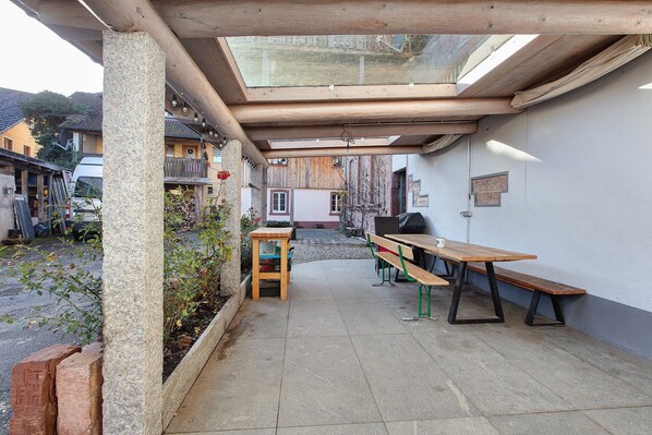 Eine Außenpatio mit einem Holztisch und Bänken, einer Glasveranda und Blick auf die Straße.