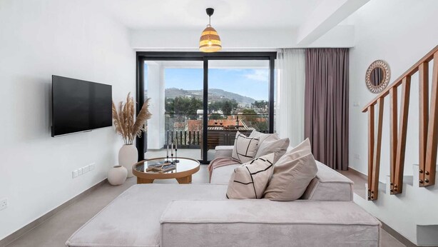 A modern living room with a sofa, a TV, a coffee table, and a view of the city. - Pamboo Ampelos House by Nomads (Paphos)
