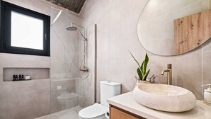 A modern bathroom with a glass-enclosed shower, a white toilet, a wooden vanity with a round mirror, and a potted plant. - Pamboo Ampelos House by Nomads (Paphos)