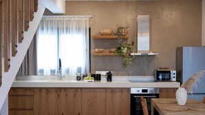 A modern kitchen with wooden cabinets, a built-in microwave, and a dining area with a table and chairs. - Pamboo Ampelos House by Nomads (Paphos)