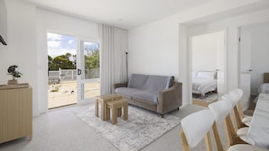 Ein modernes, helles Zimmer mit einer Couch, einem kleinen Tisch und einer Essecke mit Stühlen.