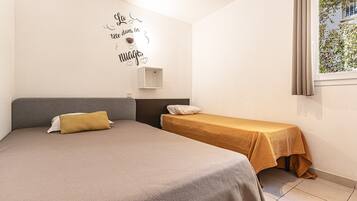 A bedroom with two beds, a wall-mounted shelf, and a window with curtains.