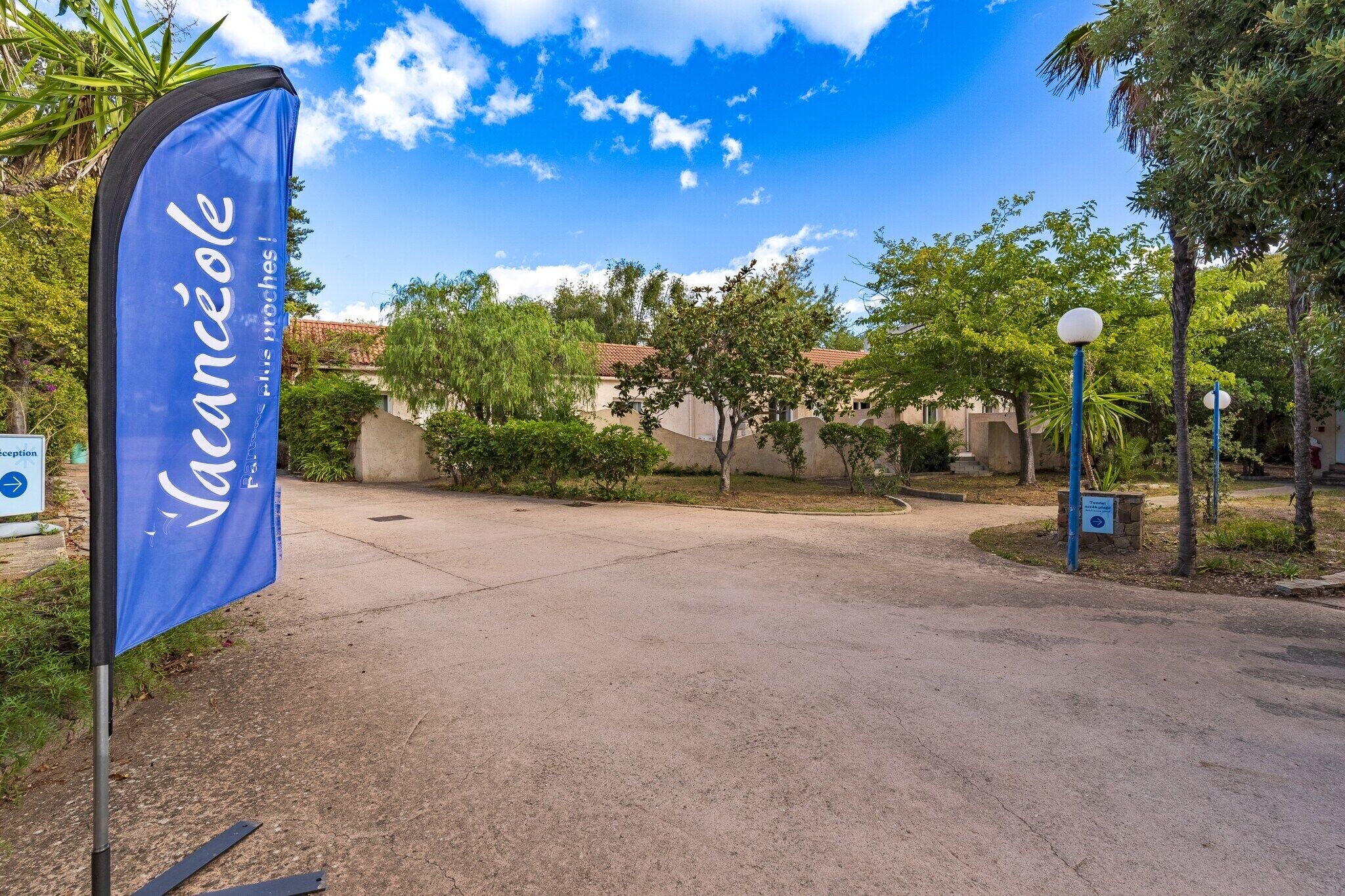 A hotel entrance with a blue flag, a clear sky, and surrounding greenery.