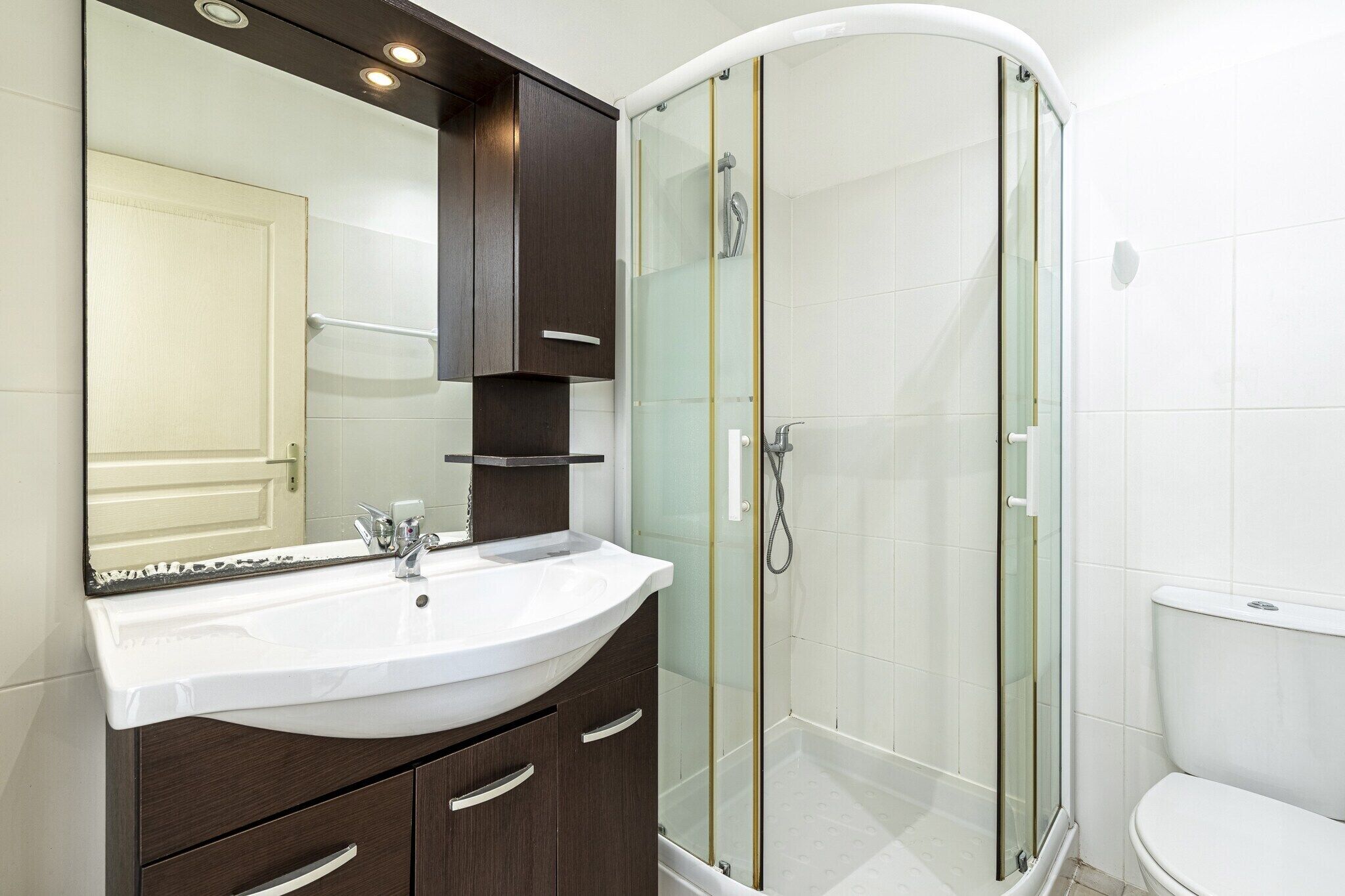 A modern bathroom with a curved shower enclosure, a white sink, and dark wooden cabinets.
