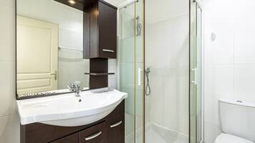 A modern bathroom with a curved shower enclosure, a white sink, and dark wooden cabinets.