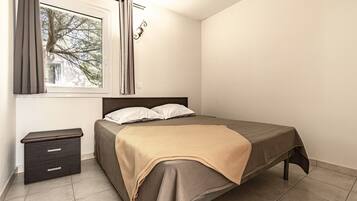 A bedroom with a bed, a nightstand, a window with curtains, and a view of trees outside.