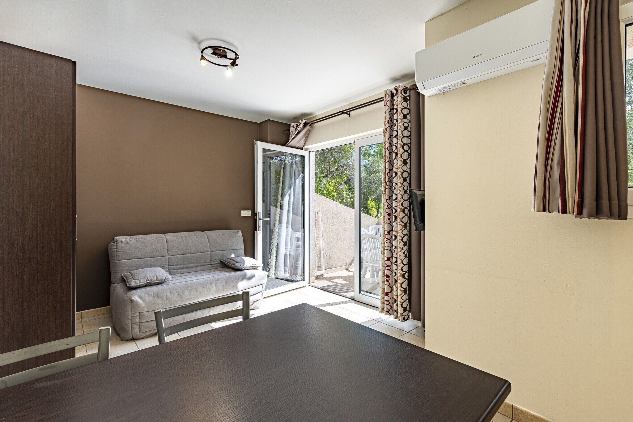 A modern room with a sofa, a dining table, and a sliding glass door leading to an outdoor area.