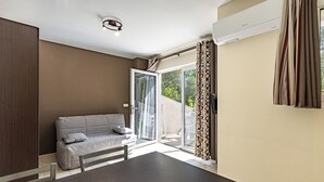 A modern room with a sofa, a dining table, and a sliding glass door leading to an outdoor area. - Coastal and Garden Living in Corsica (Sari-Solenzara)