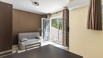 A modern room with a sofa, a dining table, and a sliding glass door leading to an outdoor area.