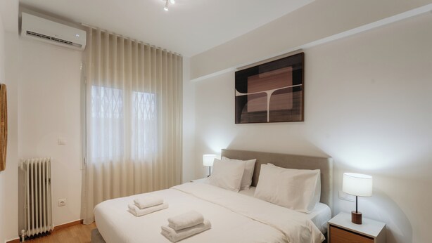 Habitación de hotel ordenada con cama, lámparas de noche, radiador y ventana con cortinas.