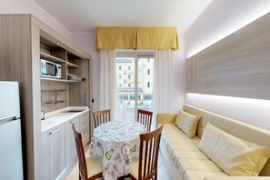 Eine kleine Küche mit Mikrowelle, Spüle und Holzausbau. Ein Esstisch mit Stühlen und eine Couch mit Kissen sind ebenfalls vorhanden.