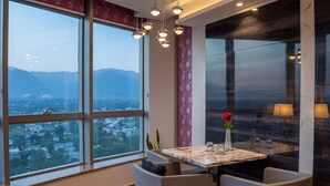 Zona pranzo moderna con tavolo, sedie e vista sulla città attraverso ampie finestre.
