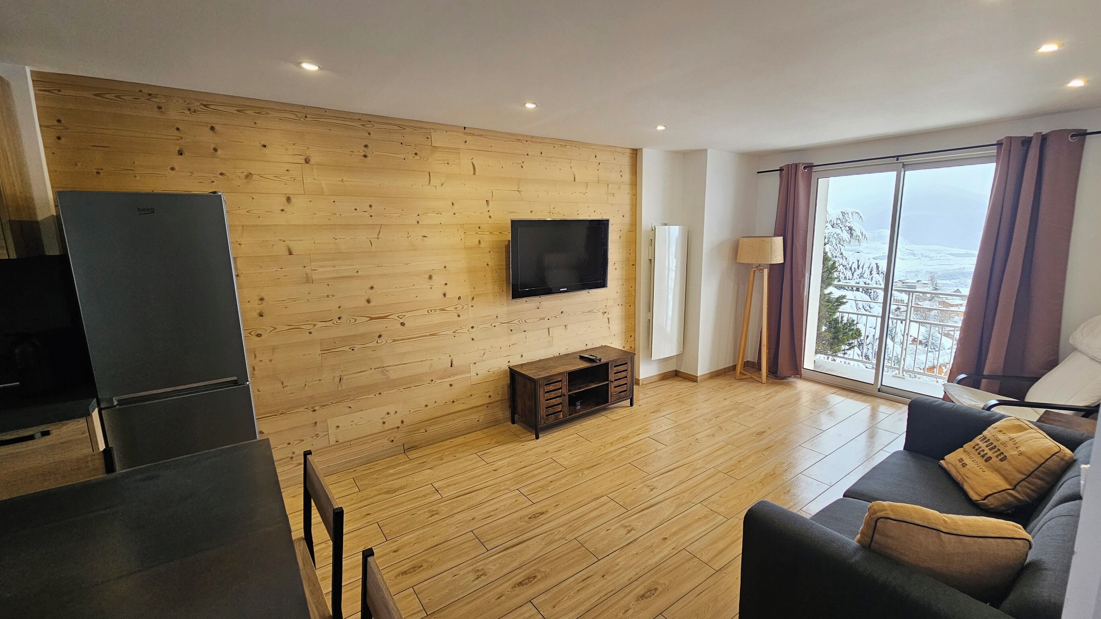 Una sala de estar moderna con una pared de madera, un televisor de pantalla plana, un sofá y vistas a un paisaje nevado a través de ventanas amplias.