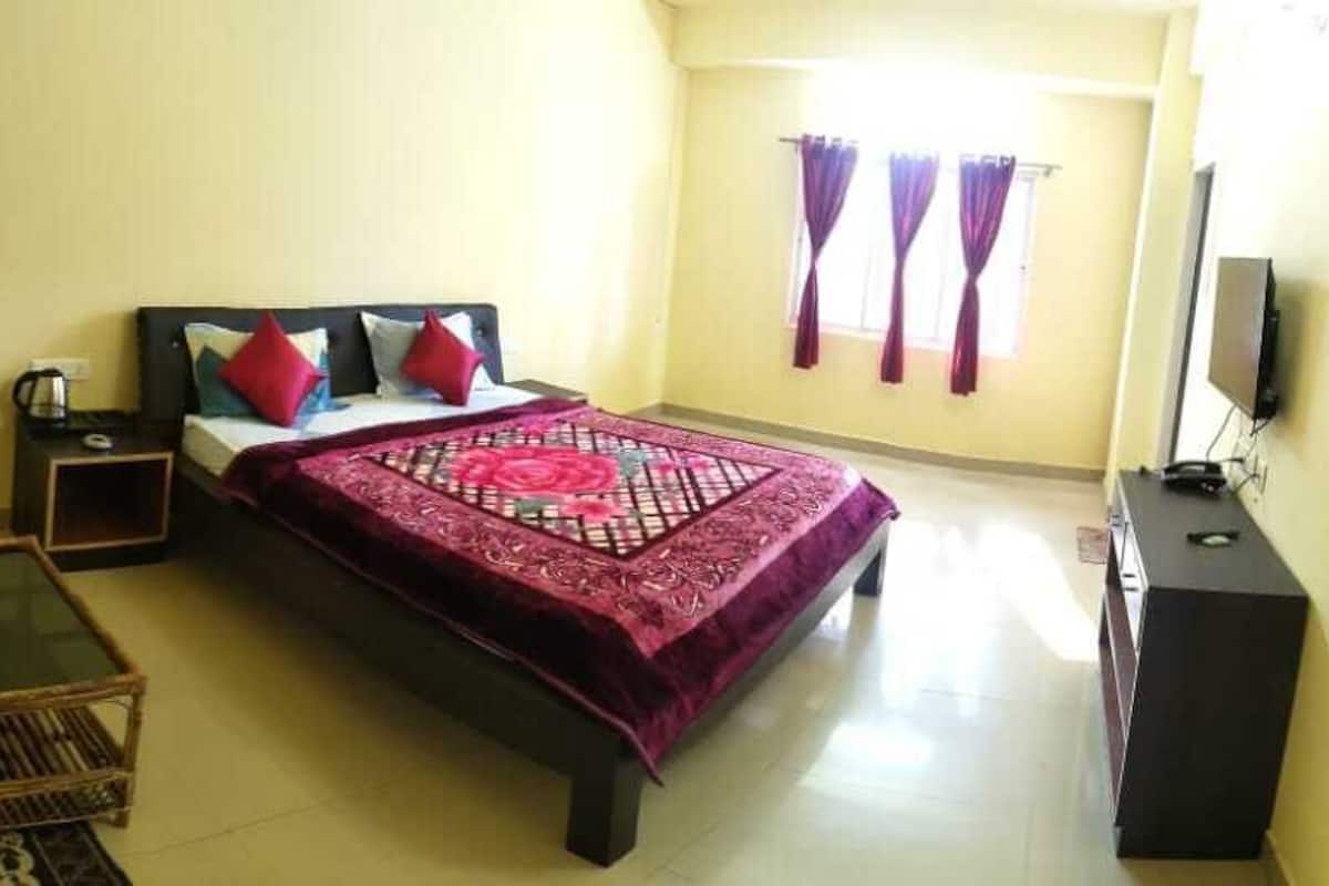 A bedroom with a bed, a nightstand, a chair, a small table, and a TV.