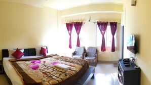 A bedroom with a bed, a chair, a desk, and a TV. - D'BONN INN (Shillong)