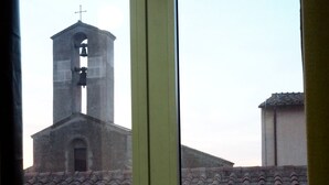 Une vue sur le clocher d’une église, avec une cloche et une croix, à travers une fenêtre dotée d’un cadre vert.