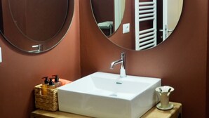 Une salle de bain avec un lavabo blanc, deux miroirs ronds et un porte-serviettes.