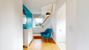 Um interior moderno com escada, uma cadeira azul e um armário branco.