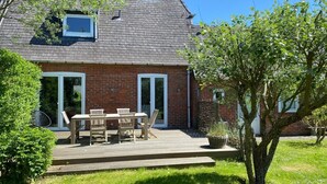 Uma casa com fachada de tijolos, um deck de madeira e uma área de varanda com mesa e cadeiras.