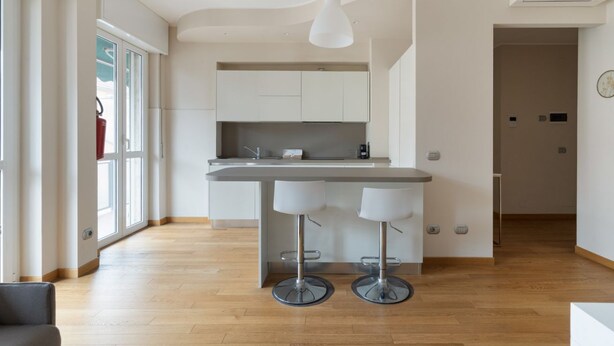 Een moderne keuken met een centraal eiland, barkrukken en een hanglamp.