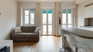 Een moderne woonkamer met een bank, een eethoek met barkrukken en grote ramen met gordijnen.