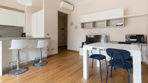 Een moderne keuken met witte kasten, een magnetron en een koffieapparaat. Er staan twee barkrukken bij een eettafel met stoelen.