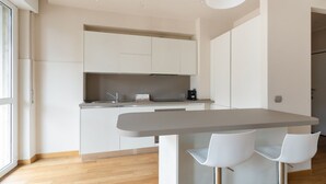 Een moderne keuken met witte kasten, een grijs aanrecht en twee witte stoelen.
