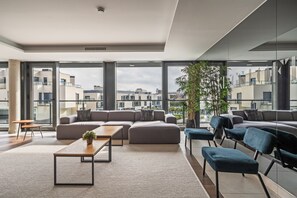 A modern lounge area with large windows, a sectional sofa, a coffee table, and a potted plant. - The Kings Residence: Business Ready alquiler temporal (San Sebastián de los Reyes)