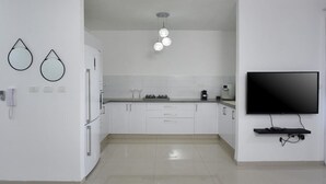 A modern kitchen with white cabinets, a flat-screen TV mounted on the wall, and a pendant light fixture above the counter. - Ariston  First Line Lake View (Tiberias)