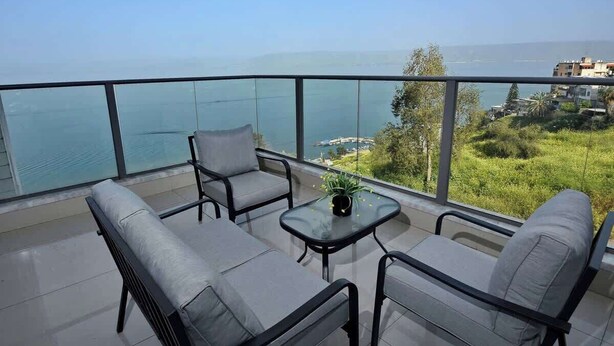 A balcony with a view of the sea and greenery, furnished with a sofa and chairs, and a small table with a plant. - Ariston  First Line Lake View (Tiberias)