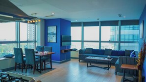 A modern living room with a dining area, large windows, and a flat-screen TV mounted on the wall. - The Grand Skyline Corner Suite (Islamabad)