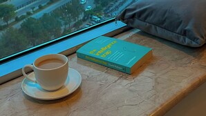 A window view of a cityscape with a book and a cup on a table. - The Grand Skyline Corner Suite (Islamabad)