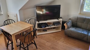 Una sala de estar con televisión, mesa de madera, sillas, sofá y ventana.