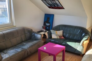Une pièce avec un canapé en cuir marron, un fauteuil en cuir vert, une table rose et une affiche accrochée au mur.