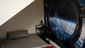 Un dormitorio con cama, mesita de noche y un mural en la pared con temática espacial.