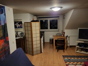 Un espace de vie compact comprenant un coin cuisine, un coin repas, un téléviseur et une grande fenêtre.