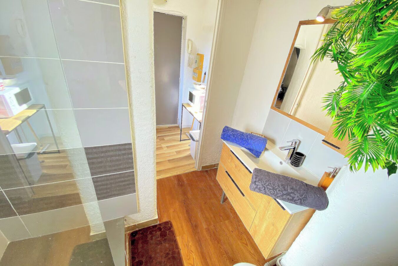 A modern bathroom with a wooden vanity, a mirror, and a plant.