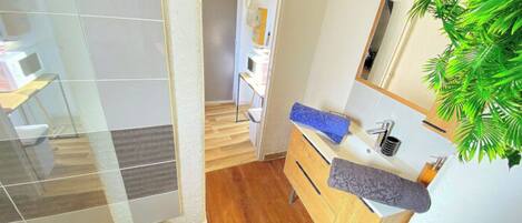 A modern bathroom with a wooden vanity, a mirror, and a plant.