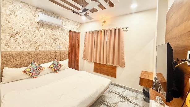 A hotel room with a bed, a ceiling fan, a TV, and a bathroom counter. - Near Mahakal Temple Hotel M L Y  Ujjain (Ujjain)