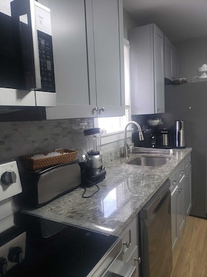 A kitchen with white cabinets, a granite countertop, a toaster, a blender, a coffee maker, and a stainless steel sink.