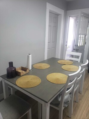 A dining table with woven placemats, a roll of paper towels, and a decorative bottle.