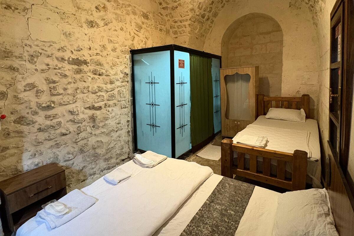 Ein rustikaler Raum mit zwei Betten, einem Holzschrank und einer Steinwand.