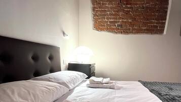 Una camera d'albergo con un particolare murale in mattoni, un letto rifatto con lenzuola bianche e una testiera.