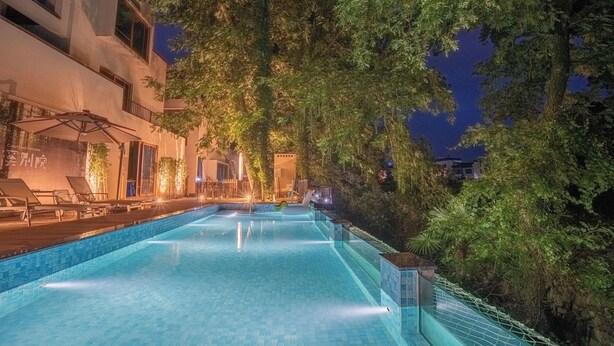 A swimming pool with a view of a building and trees at night. - Mengxi Bieyuan Forest Resort Hotel (Huangshan)