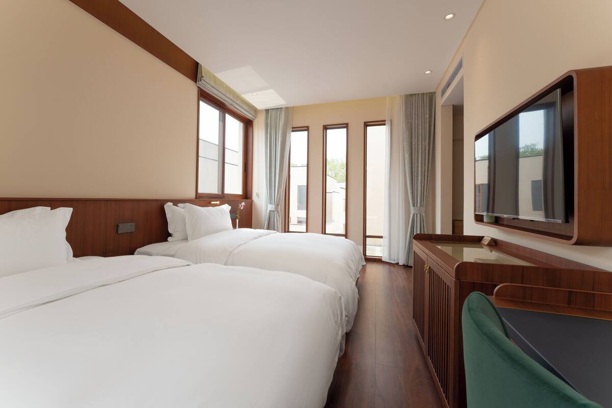 Ein Hotelzimmer mit zwei Betten, einem Fernseher und einem Fenster mit Vorhängen.