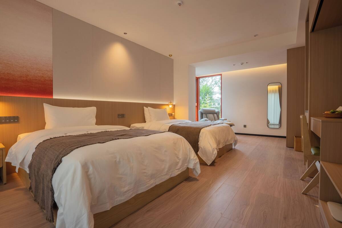 Ein modernes Hotelzimmer mit zwei Betten, Holzboden, einem großen Spiegel und Blick ins Freie.
