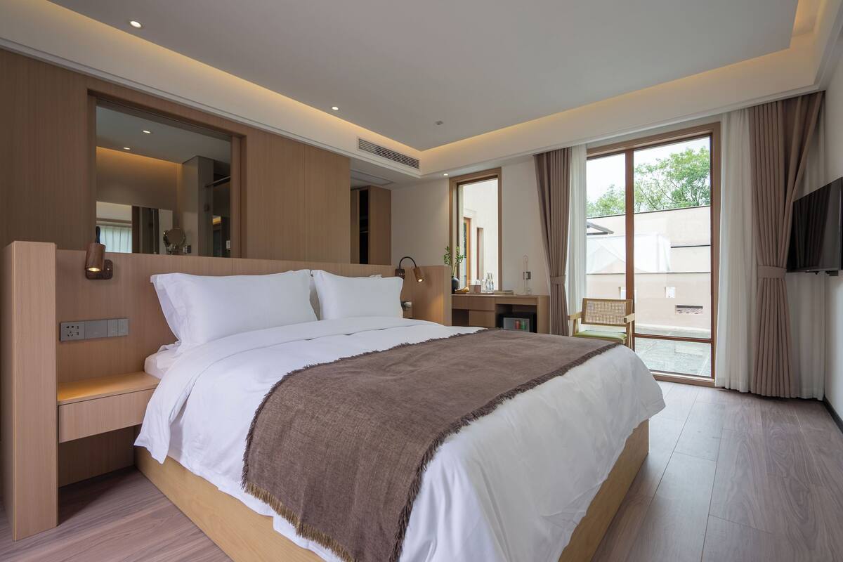 Ein modernes Hotelzimmer mit einem großen Bett, einem Nachttisch, einem Spiegel und Blick nach außen.
